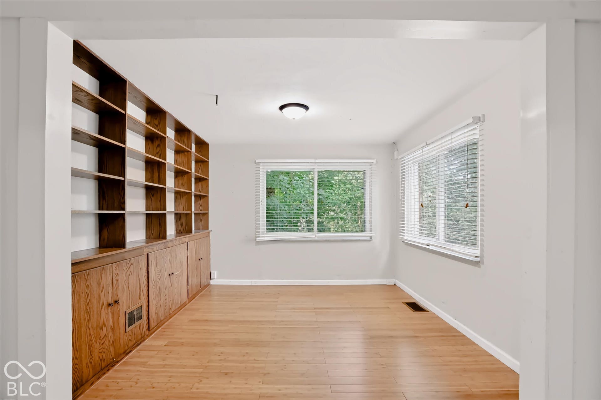 Expansive built-in shelving with lower cabinetry, wood-finish flooring, and multiple windows allowing natural light
