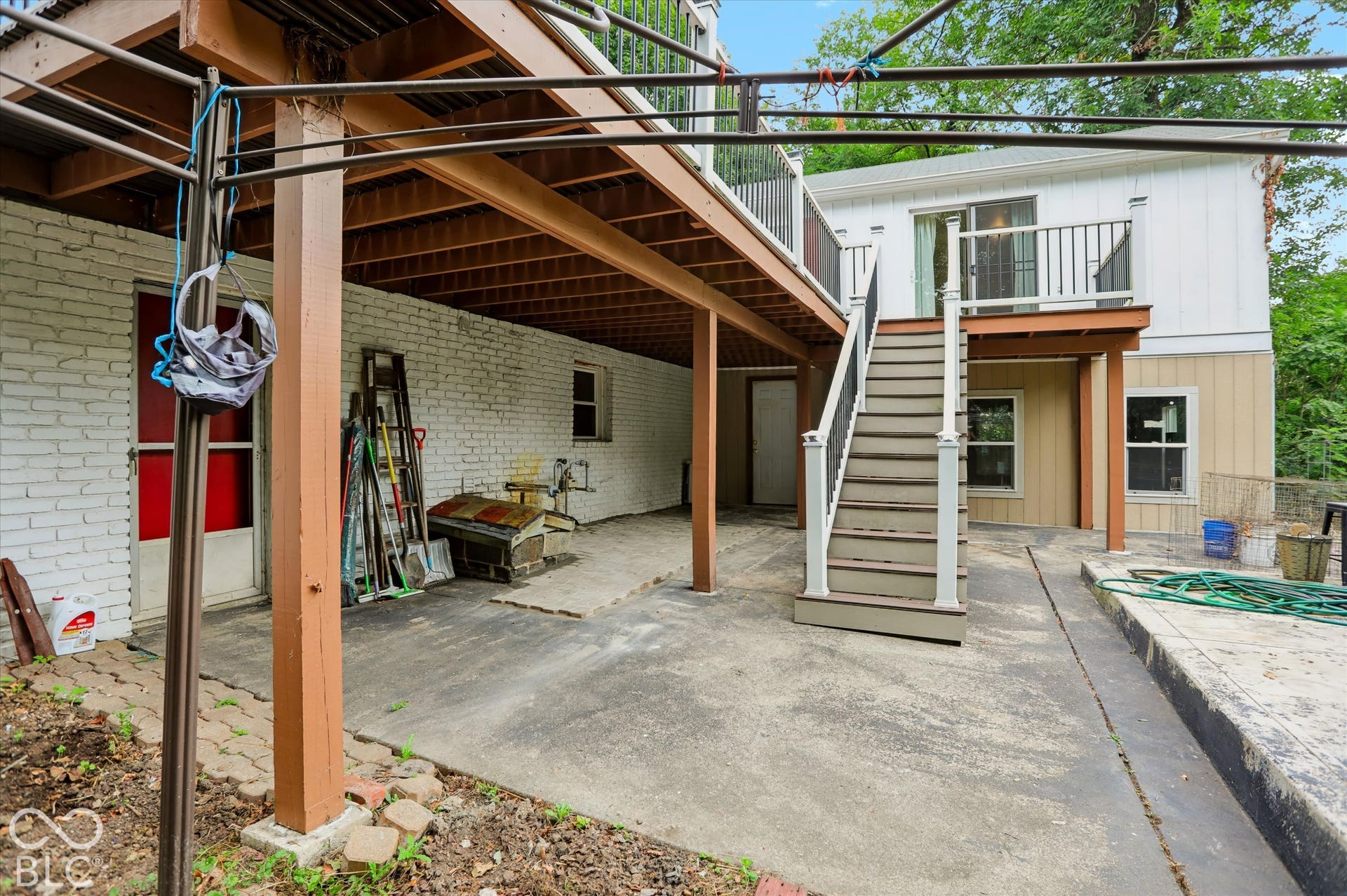 Multi-level exterior with a ground-level covered patio, an exterior staircase with dark railings, and an upper-level balcony with matching railings