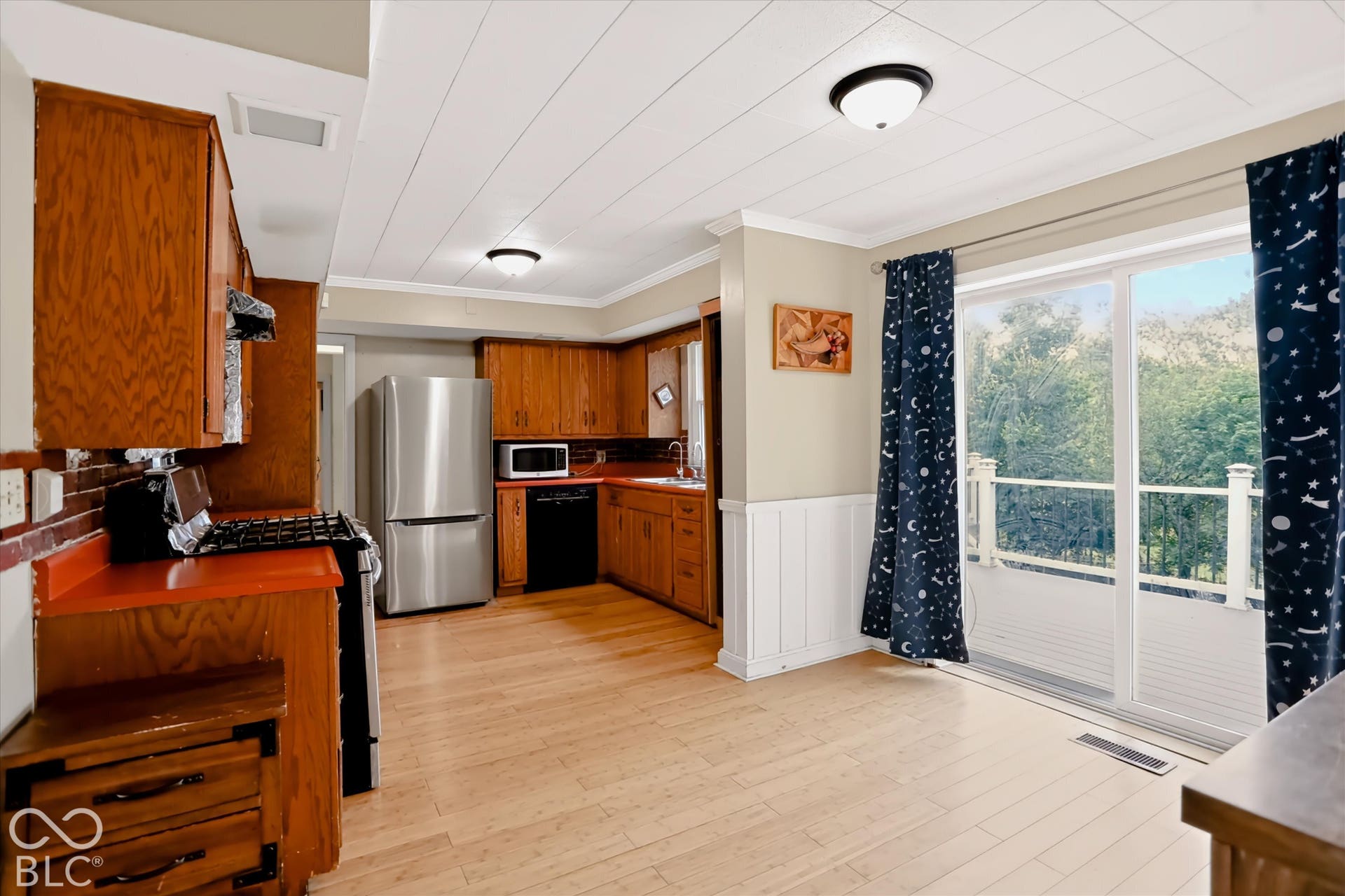 Wood-finish flooring, wood cabinetry, stainless steel refrigerator, built-in microwave, and sliding glass door to exterior