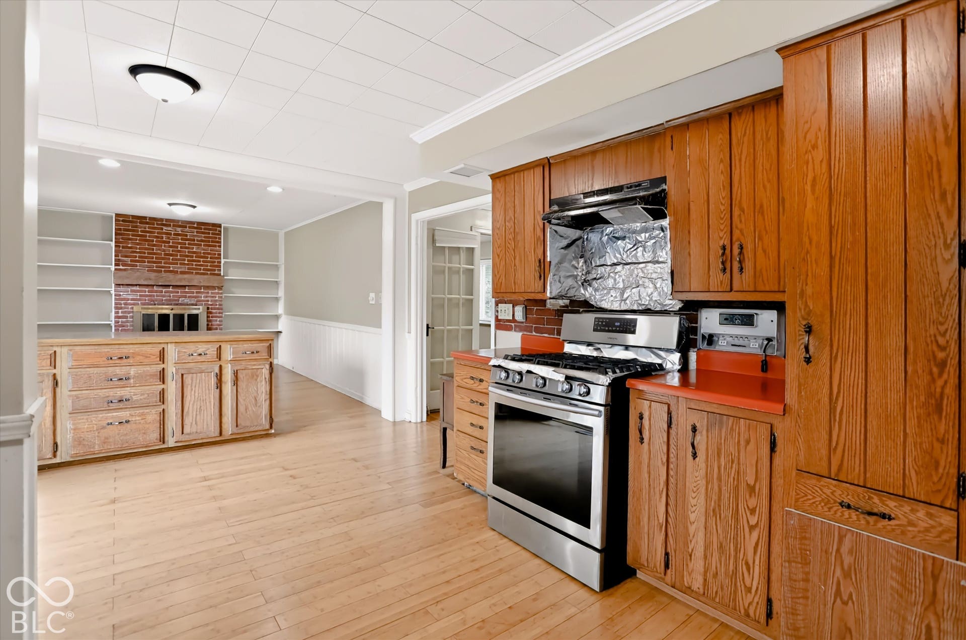 Wood-finish flooring throughout, full-height wood cabinetry, stainless steel oven with gas range, brick accent wall, and built-in shelving