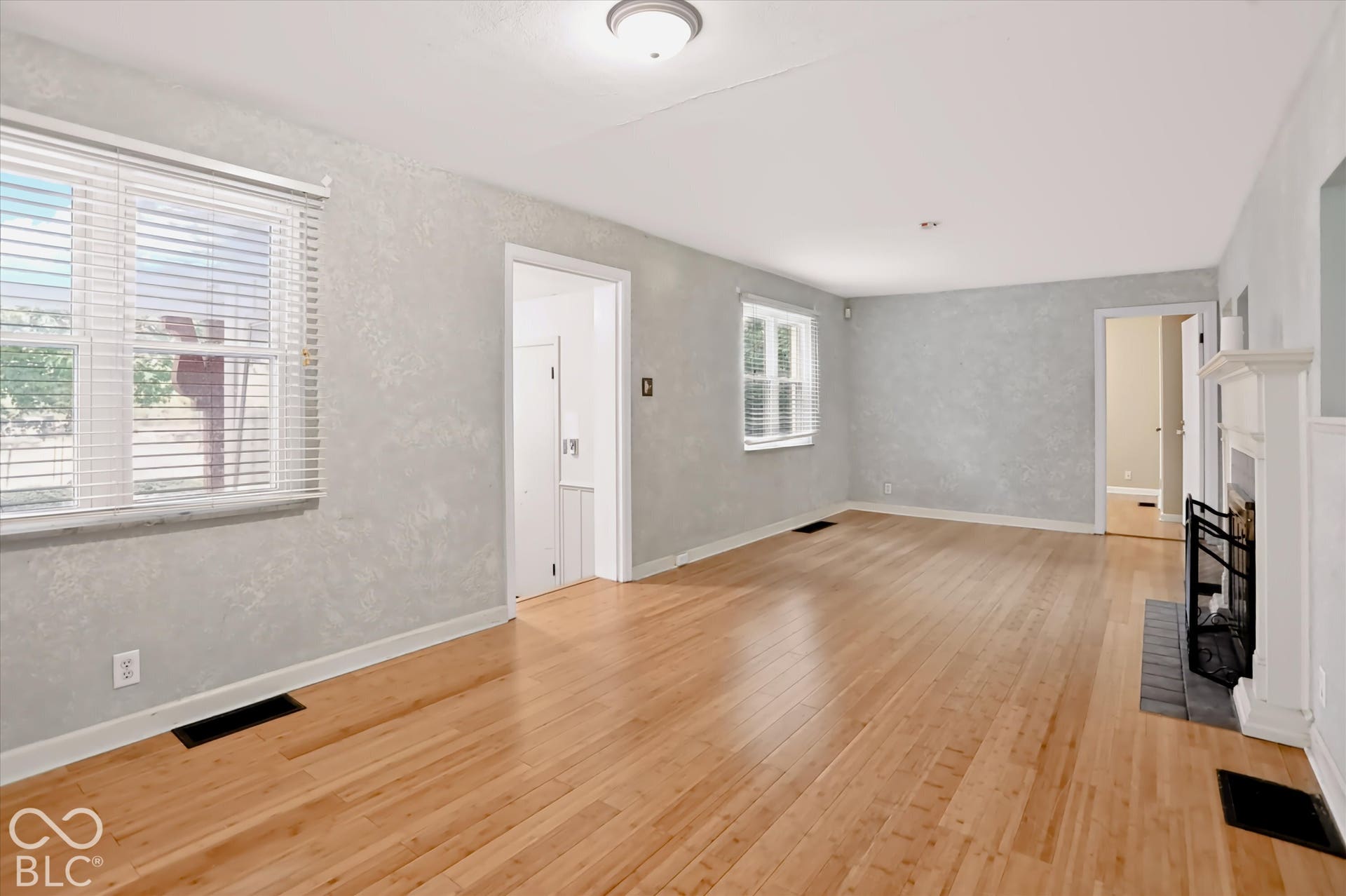 Hardwood flooring, painted walls, windows with blinds, and a built-in fireplace with a mantel