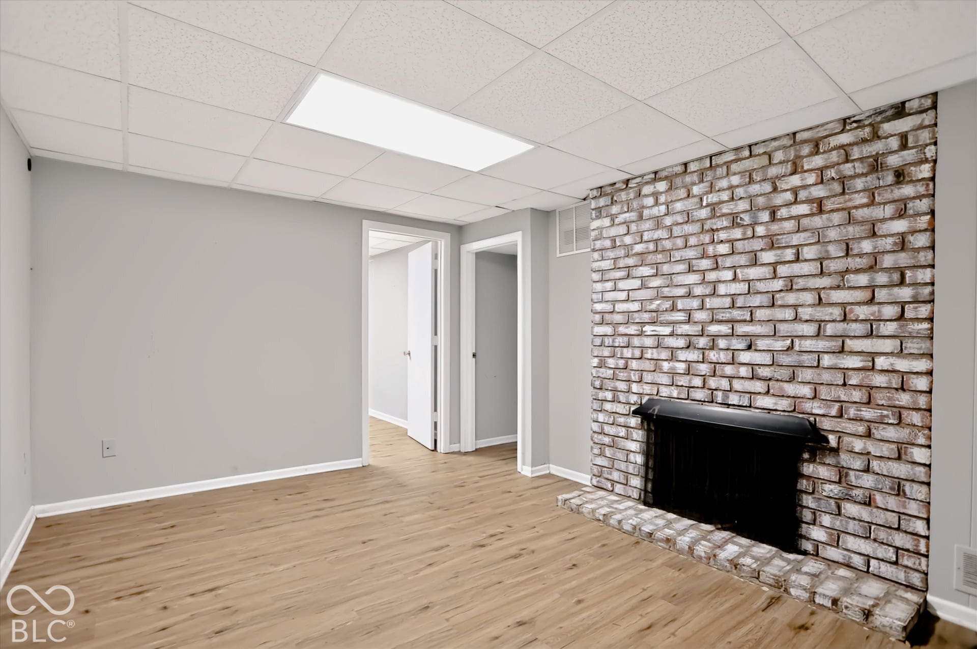 Exposed brick fireplace with a black metal firebox, wood-finish flooring, and drop panel ceiling