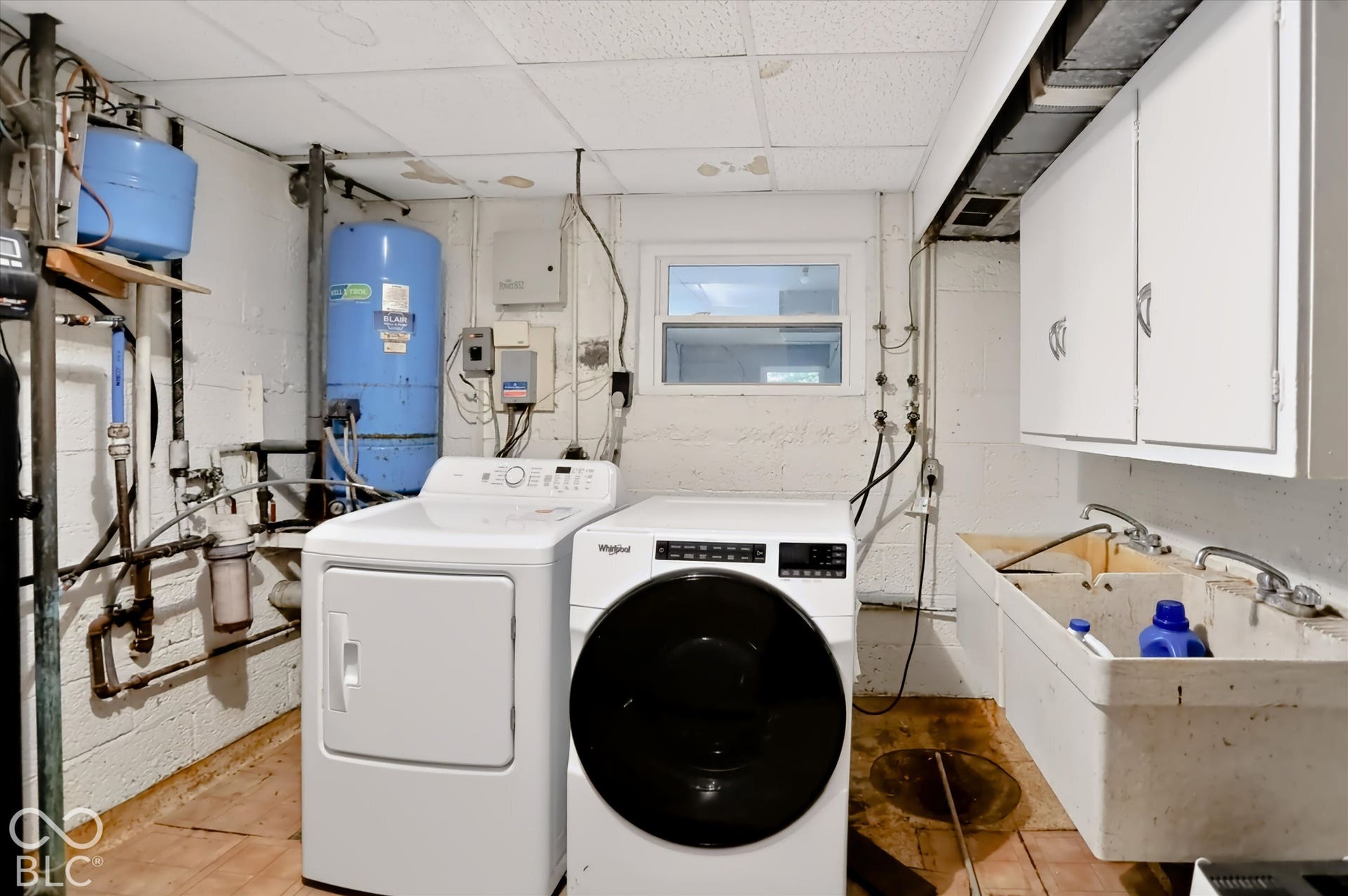 Laundry area with a utility sink, white upper cabinets, and a window
