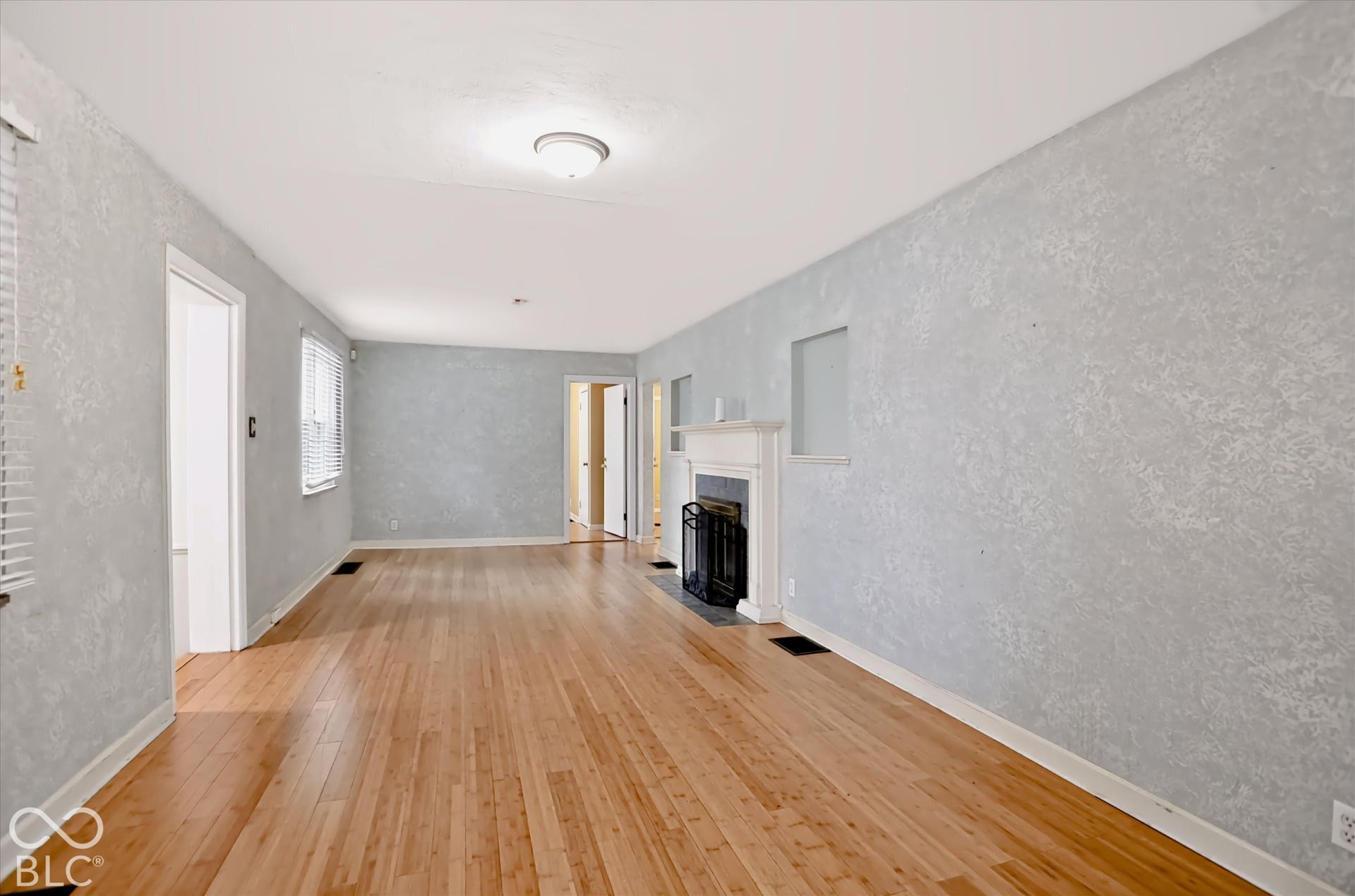 Hardwood flooring, white window blinds, fireplace with white mantel, white trim, and light-colored walls