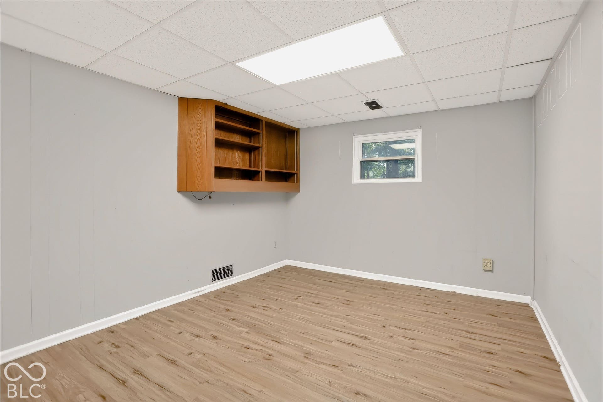 Wood-finish flooring, light gray walls, built-in shelving, white trim, and a drop ceiling with recessed lighting