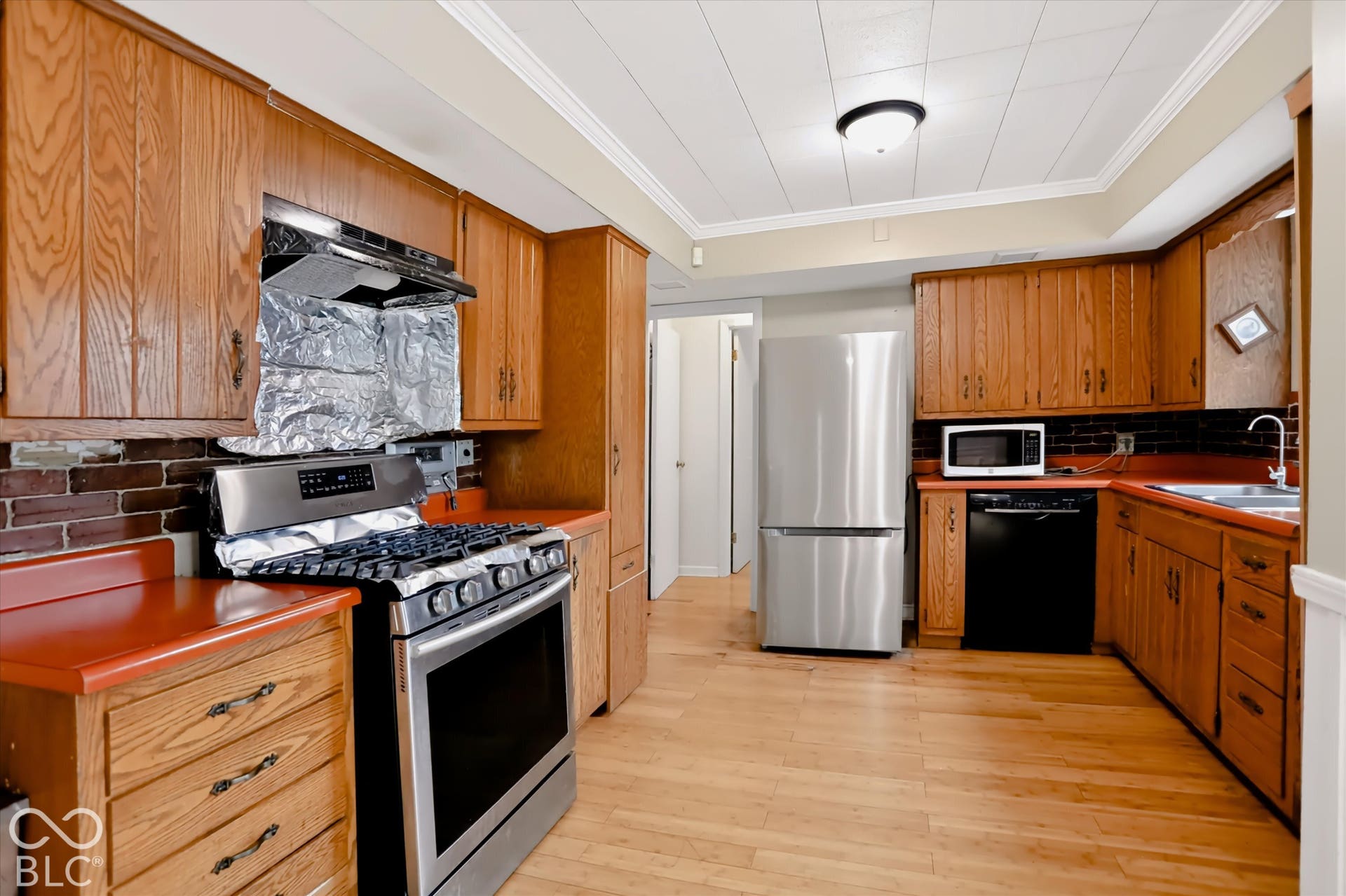 Wood-finish flooring, ample wood cabinetry, stainless steel refrigerator, stainless steel range, and ceiling-mounted light fixture
