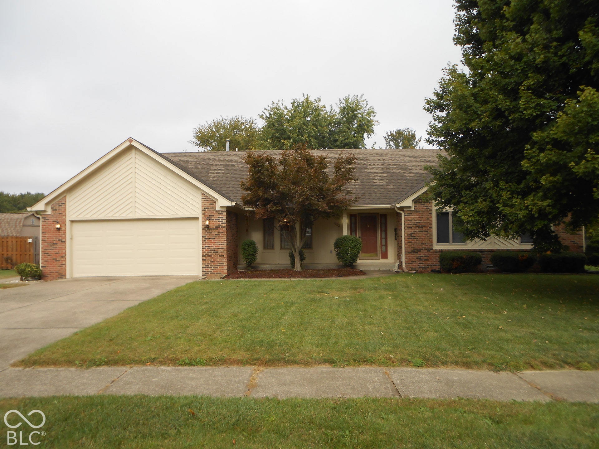 Brick and siding exterior with an attached garage, concrete driveway, and mature landscaping