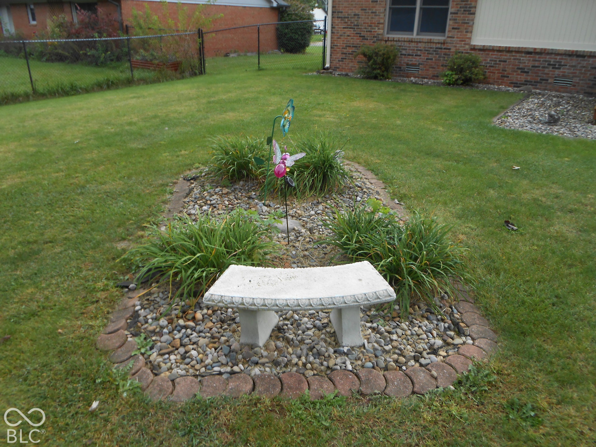 Landscaped garden bed with decorative stone, low-maintenance plantings, and a stone bench
