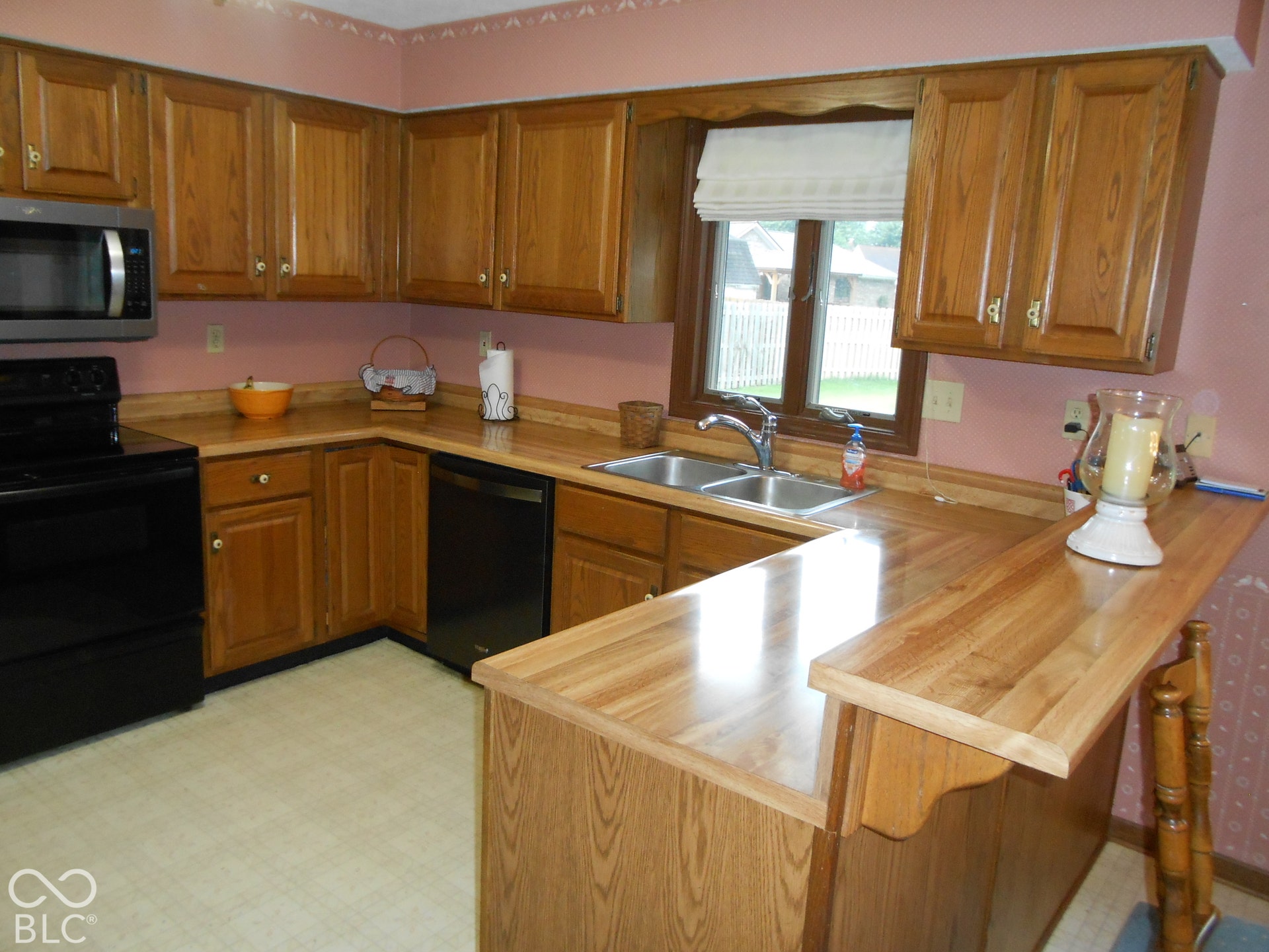 L-shaped counter space with wood-finish surface, stainless steel sink, wood cabinetry.