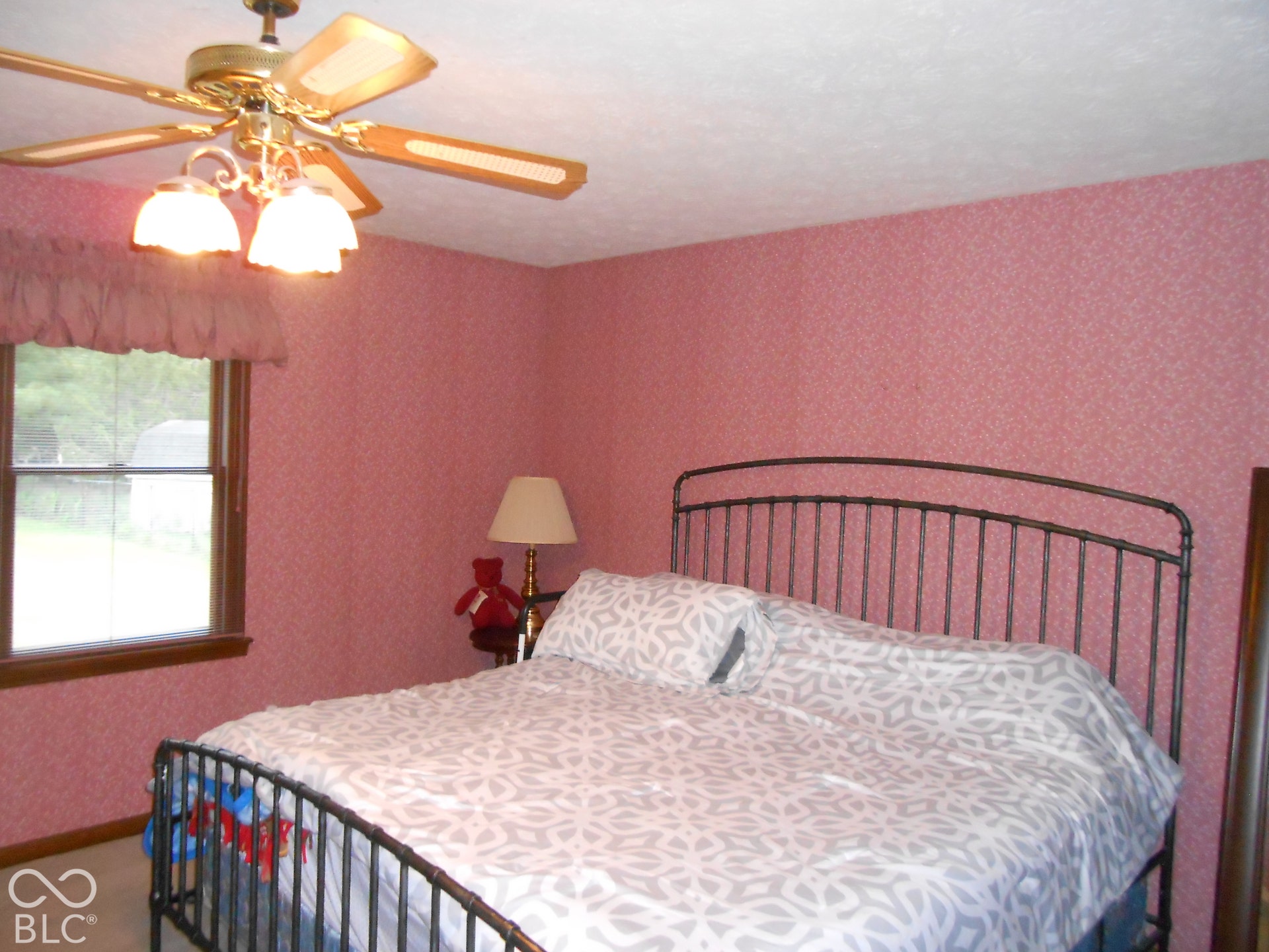 Ceiling fan with integrated lighting, wood-trim window, patterned wall covering, carpet flooring.