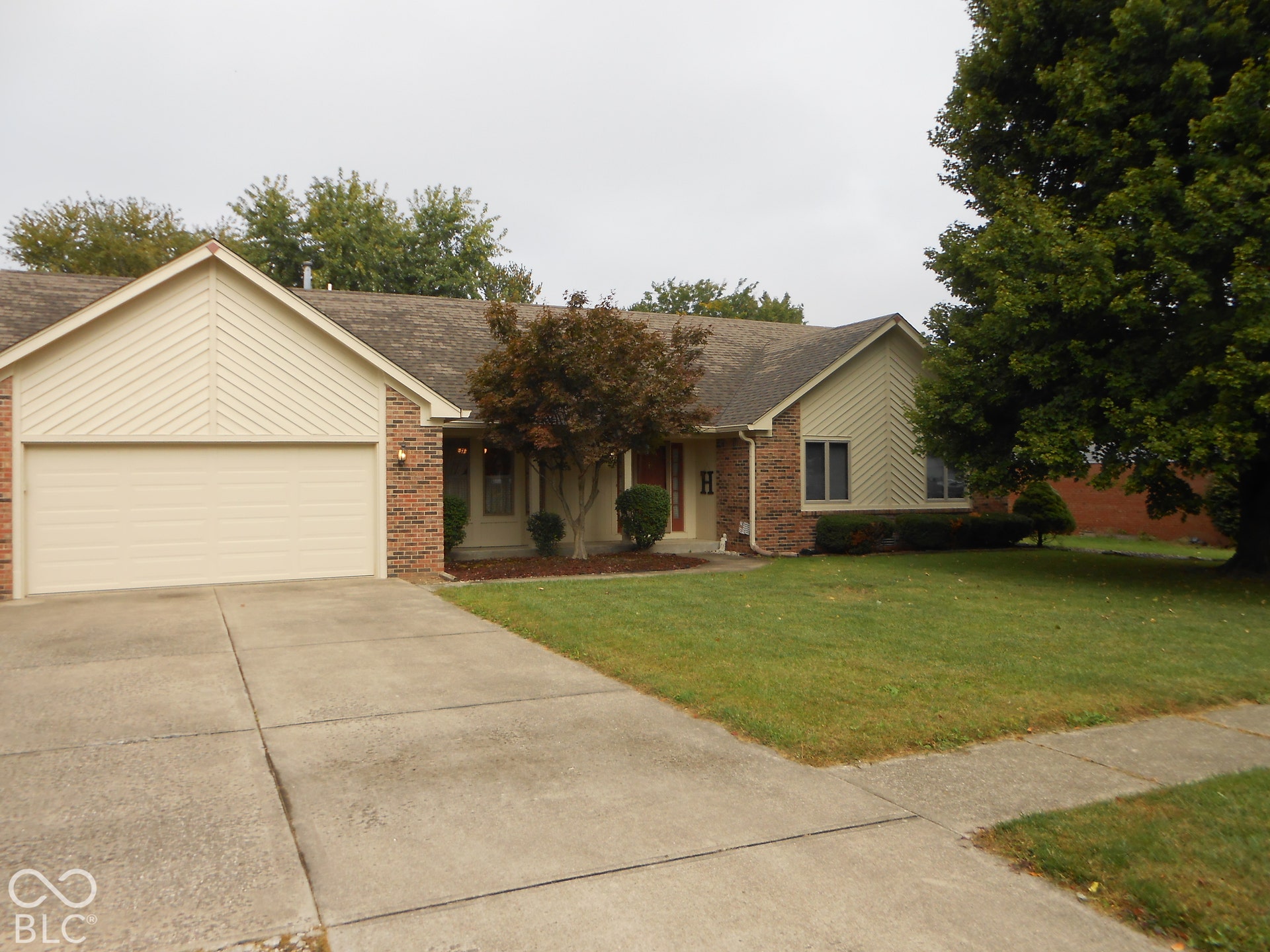 Brick and siding exterior with an attached garage, concrete driveway with extra parking spaces and mature landscaping