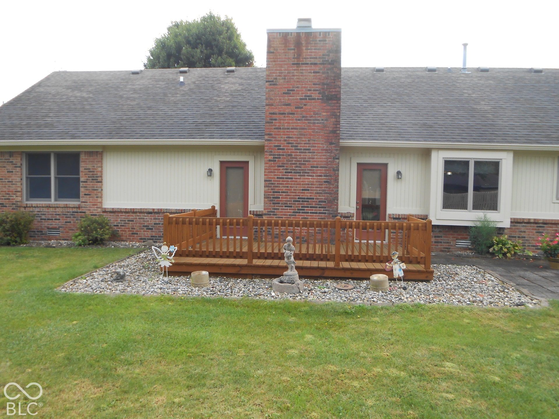 Expansive lawn with a wooden deck, brick chimney, and multiple windows