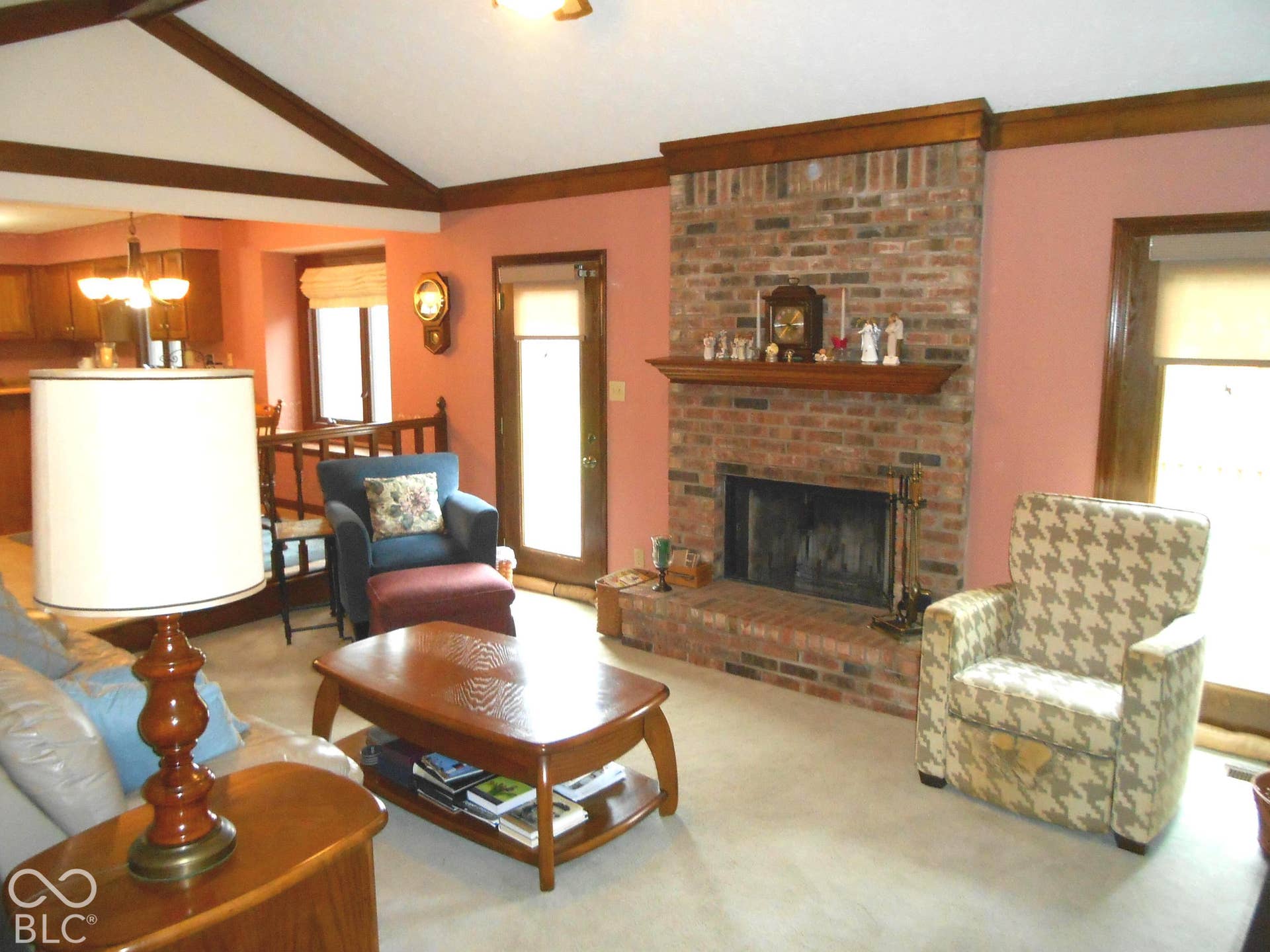 Brick fireplace with wood mantle, vaulted ceiling with exposed wood beams, and a wood-finish door with glass panel