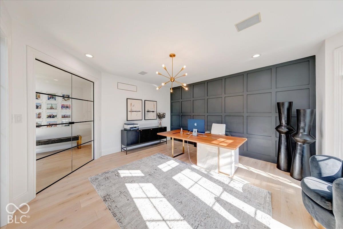 Light wood-finish flooring, two-panel glass entry doors with black framing, accent wall with square paneling, recessed lighting, and a sputnik-style chandelier