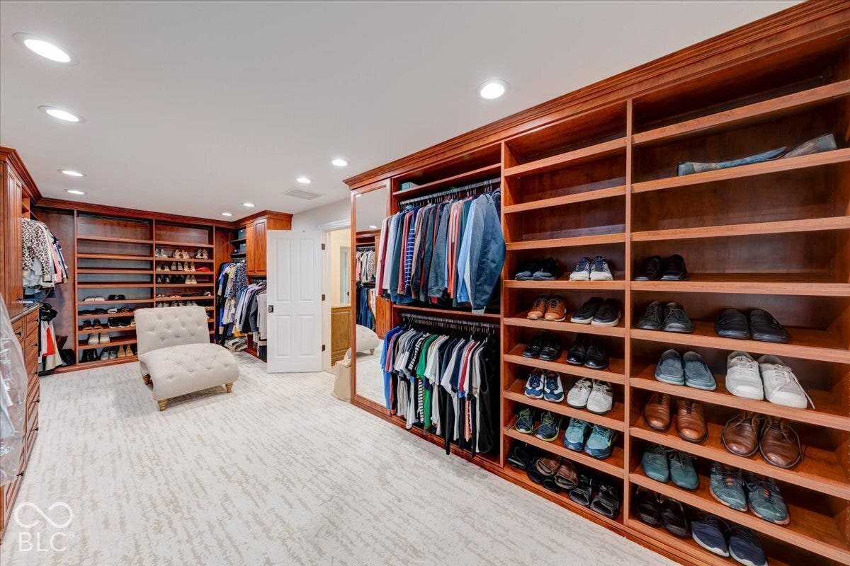 Luxurious walk-in closet featuring custom wood-finish cabinetry with extensive shelving and hanging storage, light wood flooring, recessed ceiling lighting, and organized display areas for footwear and accessories throughout the space