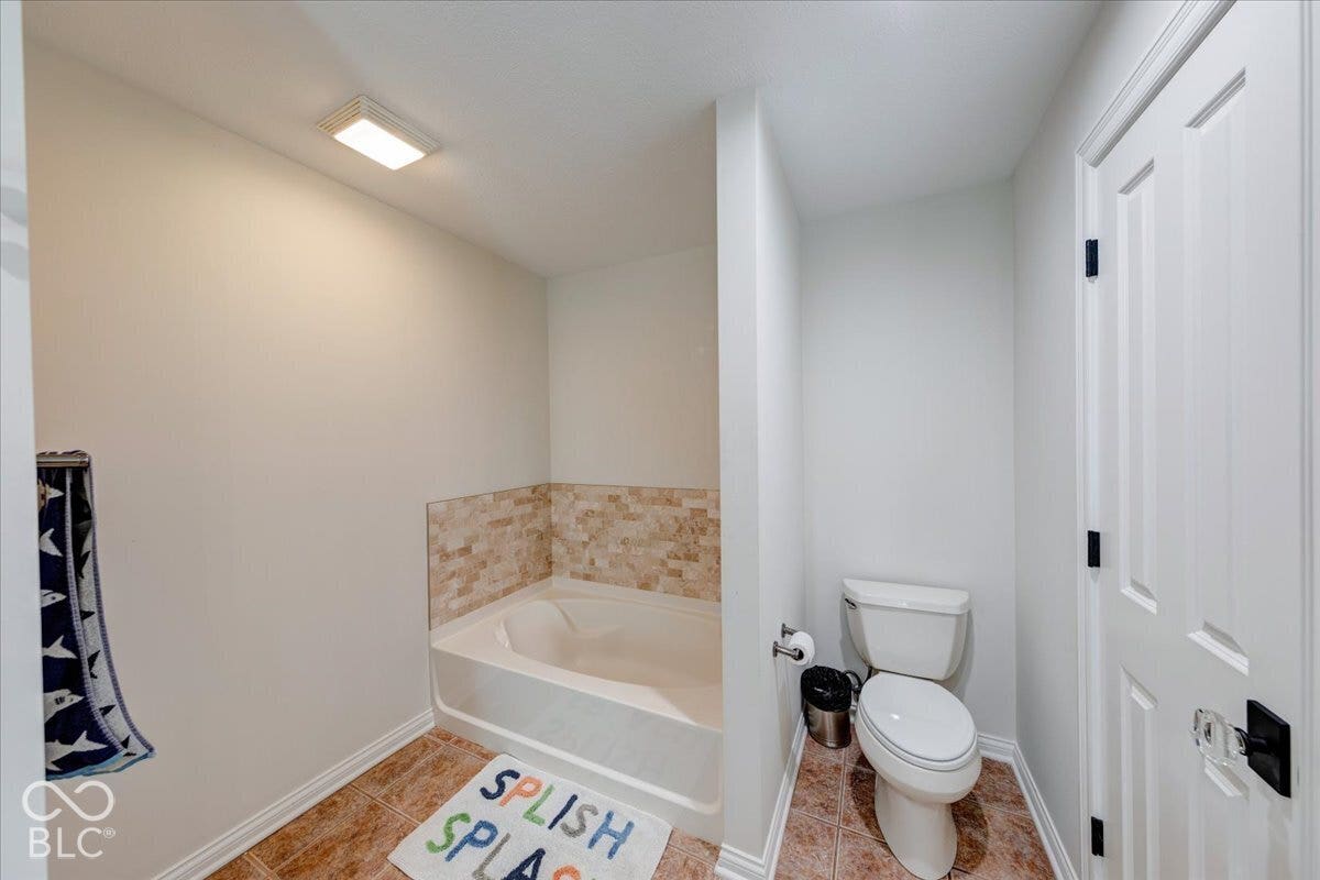 Functional full bathroom featuring a soaking tub with tile surround, ceramic toilet, wood-finish flooring, and recessed ceiling lighting