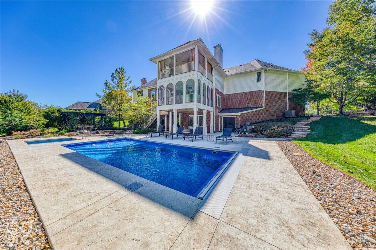 Expansive backyard featuring a rectangular swimming pool, an integrated spa, a stamped concrete patio, and tiered landscaping with stone steps