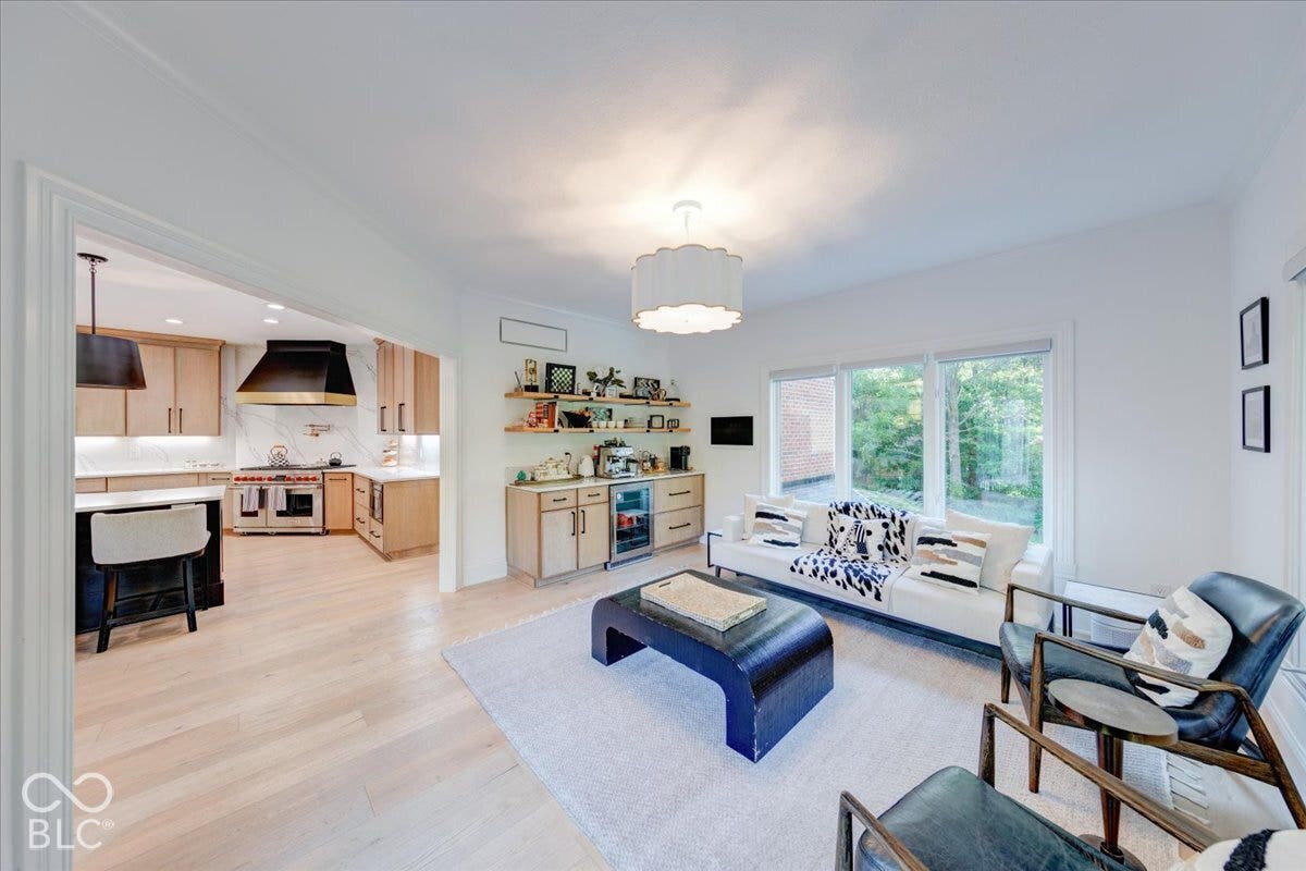 Light wood-finish flooring throughout, recessed lighting, expansive windows, built-in bar cabinetry with beverage refrigerator, and a kitchen featuring a large range with a custom hood