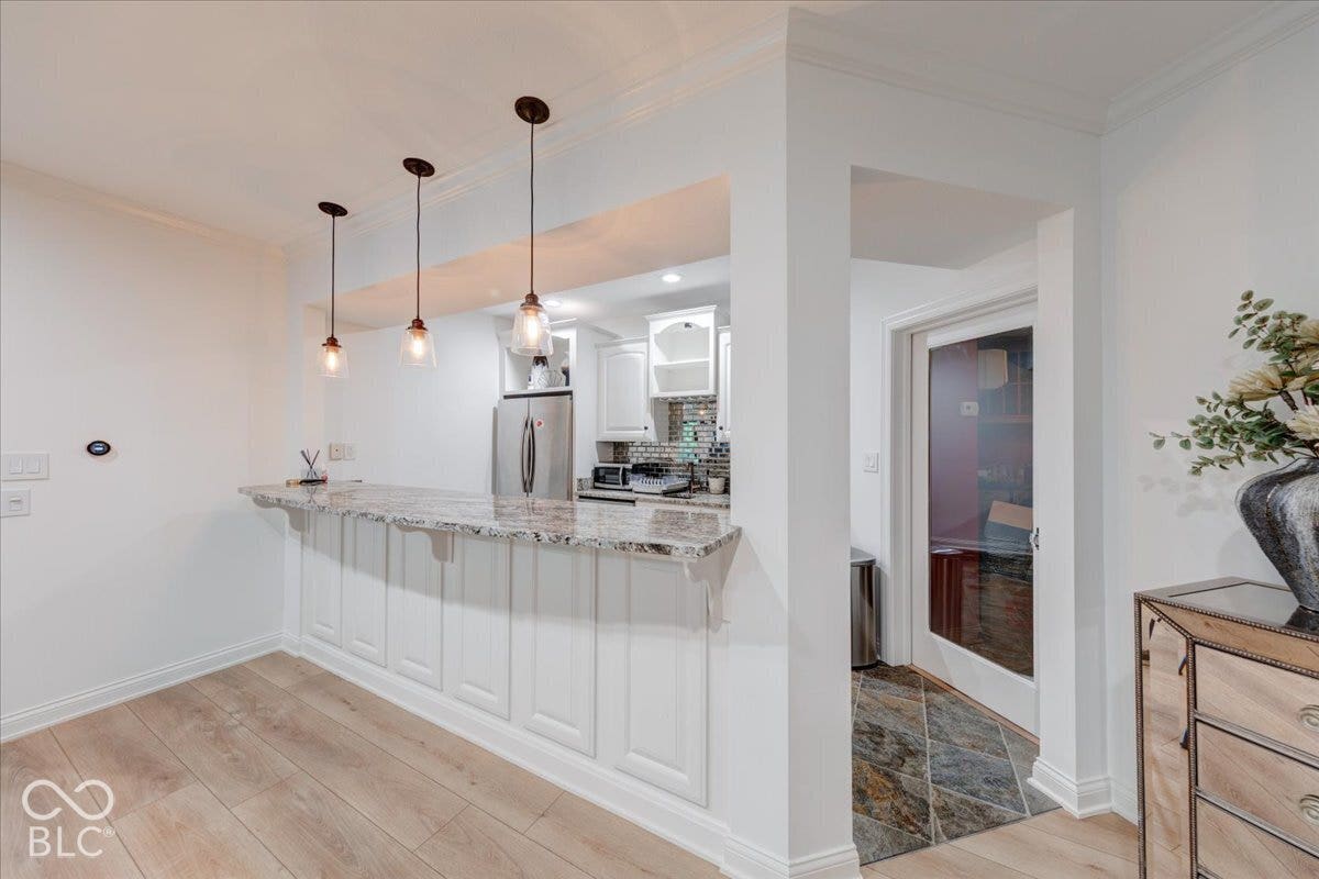 Kitchen pass-through with granite countertop, integrated white cabinetry, and pendant lighting