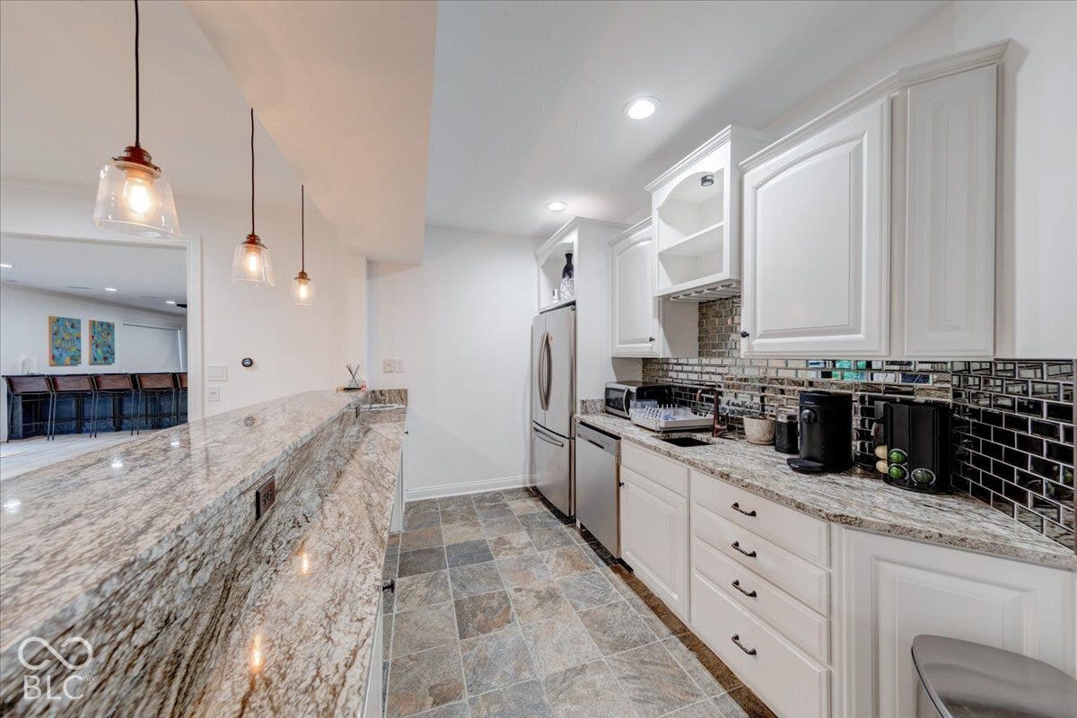 White cabinetry with dark hardware, stone-finish countertops, stainless steel appliances, and a tiled backsplash