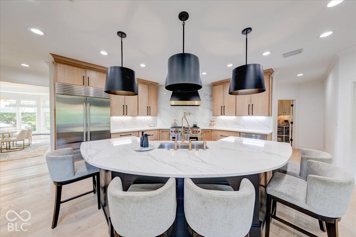 Gourmet kitchen with a large curved island, natural wood cabinetry, integrated stainless steel refrigerator, and a statement range hood