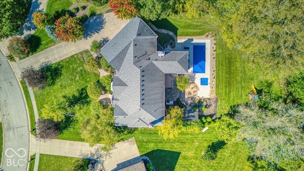 Expansive property featuring a multi-gabled roofline, concrete driveway, lush green lawn, mature trees, and a rectangular swimming pool with an integrated spa