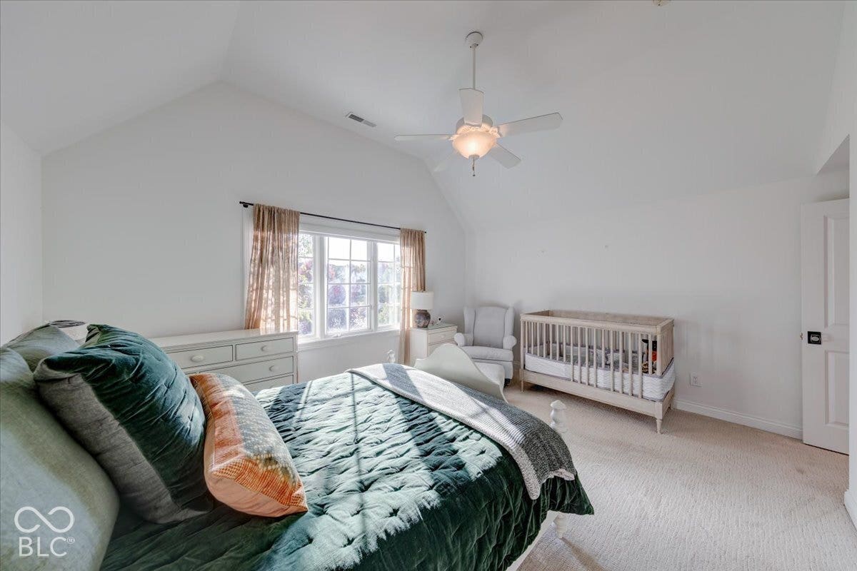 Vaulted ceiling with a ceiling fan, broad window with multiple panes, and light-toned carpet flooring