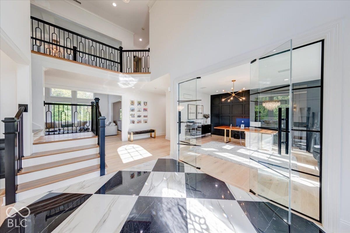 Two-story foyer with black and white checkered flooring, hardwood staircase with black wrought iron railing, and glass-paneled office entrance