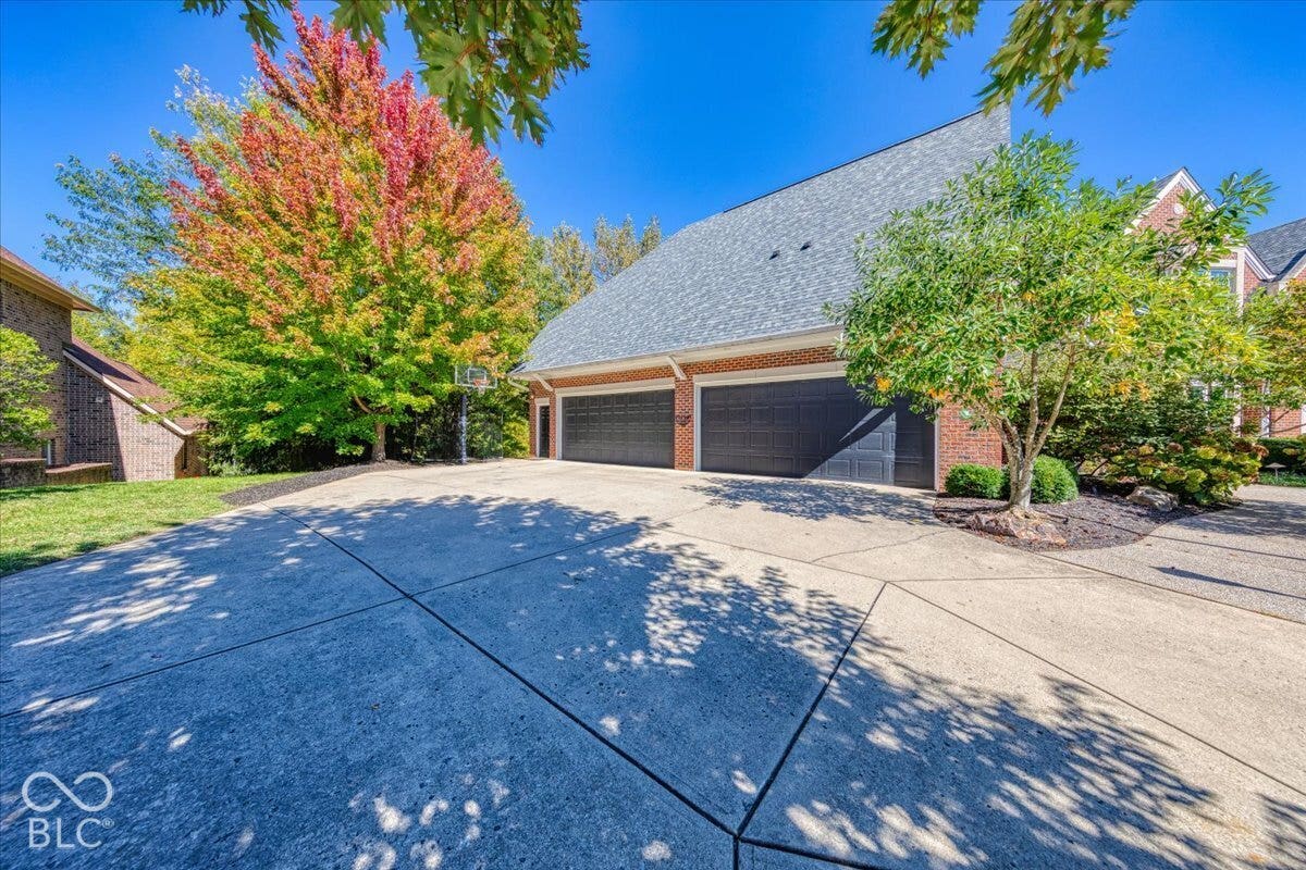 Brick exterior with a multi-car garage, concrete driveway, and mature landscaping