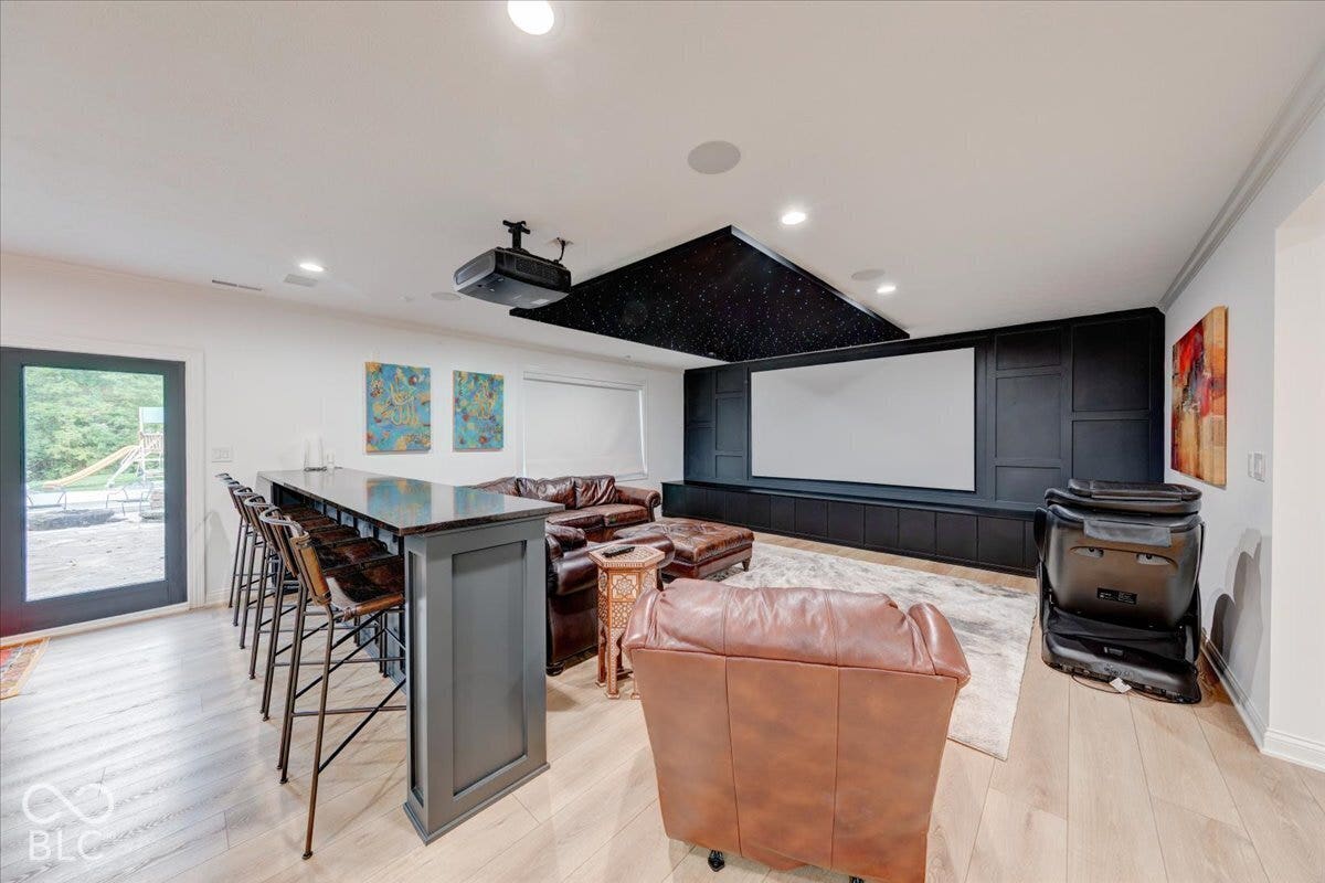 Hardwood-finish flooring throughout, media room with projection screen, built-in cabinetry, recessed lighting, and a beverage bar with dark countertop