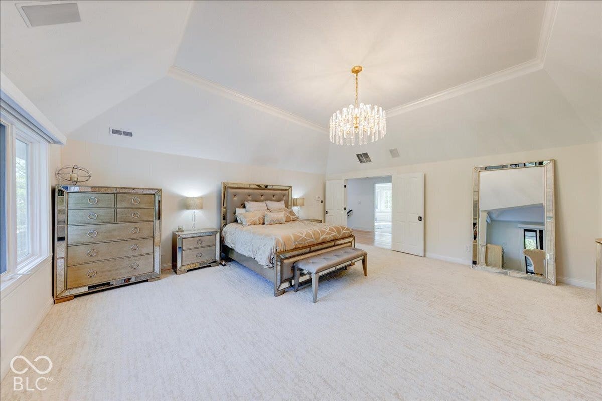 Vaulted ceiling with crown molding, crystal chandelier, and neutral carpeting