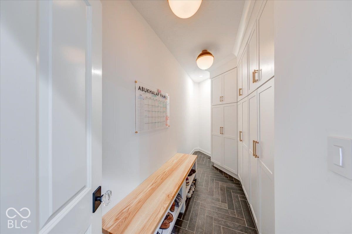White built-in cabinetry with gold-finish hardware, wood-finish herringbone flooring, and a light wood-finish bench