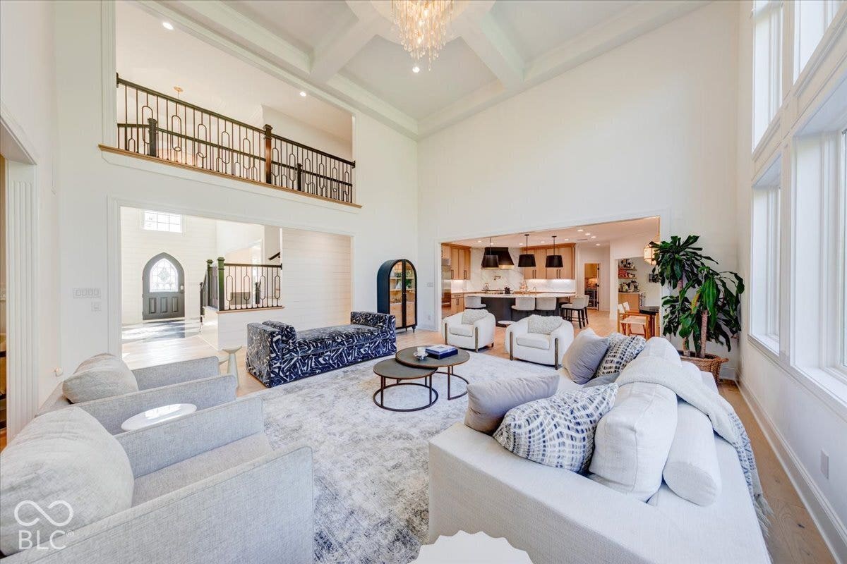 Double-height living area with coffered ceilings, hardwood flooring, and abundant natural light from multiple windows
