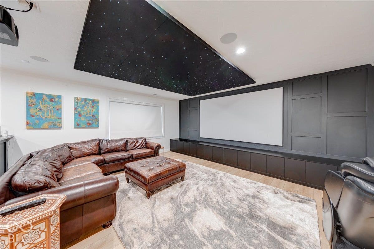Home Theater featuring a starlit ceiling with recessed lighting, a curved leather sectional sofa, a large projection screen with dark paneled surround, plush area rug, and decorative wall art
