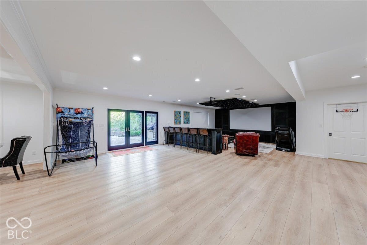 Spacious recreation area featuring wood-finish flooring, recessed lighting, and a built-in wet bar with seating