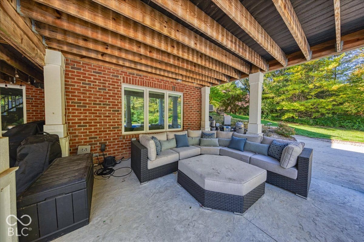 Covered patio with stamped concrete flooring, brick exterior, white columns, and wood ceiling