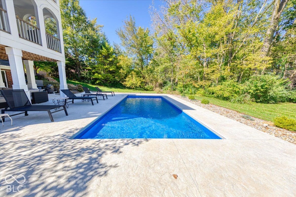 In-ground swimming pool with a concrete surround, bordered by a manicured lawn and mature trees