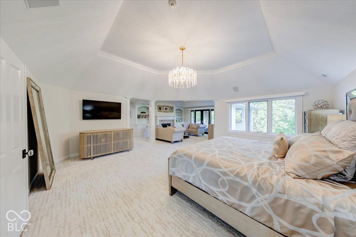 Tray ceiling with crown molding, chandelier, multiple windows, built-in shelving, and a wall-mounted display