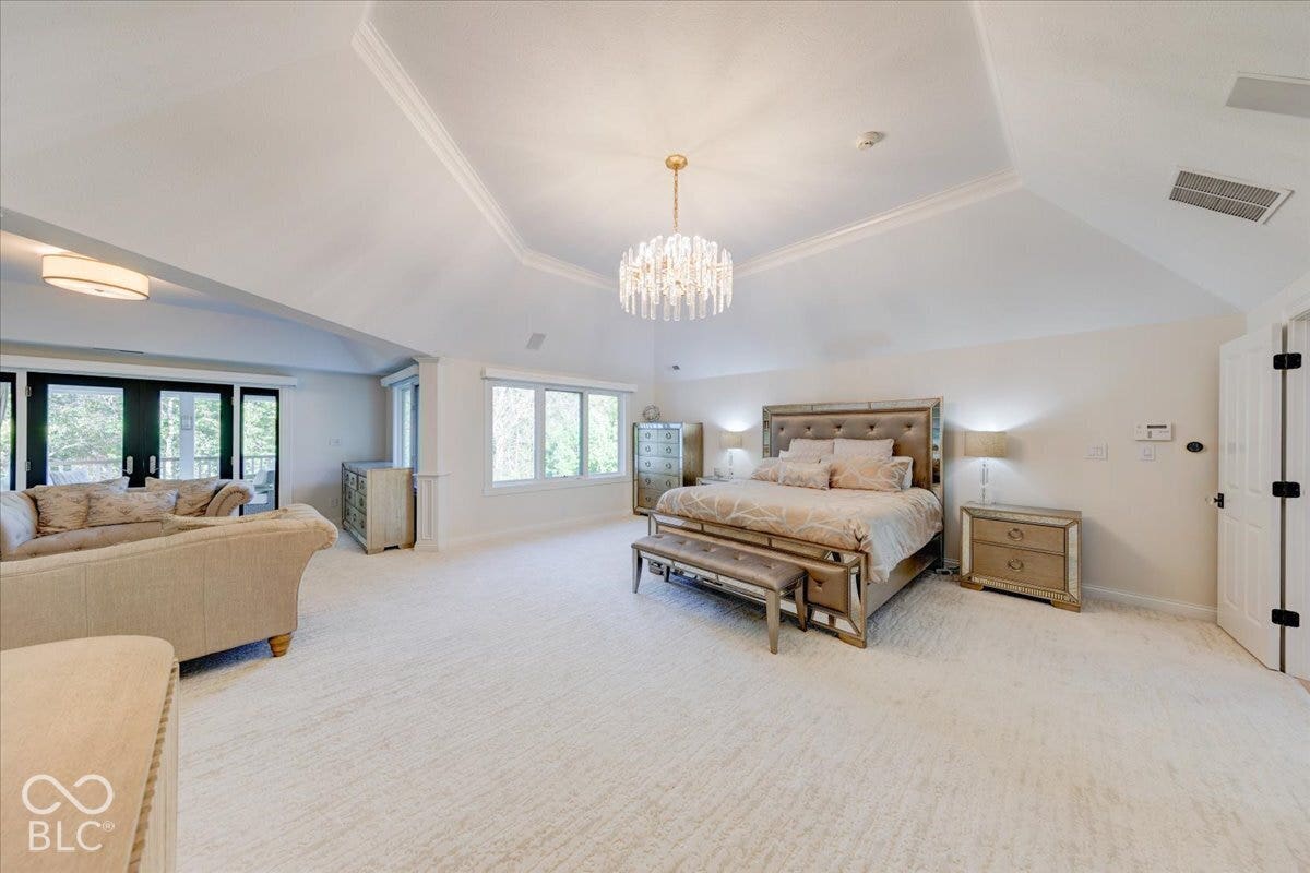 Vaulted ceiling with crown molding, chandelier, white carpet flooring, multiple windows, and French doors