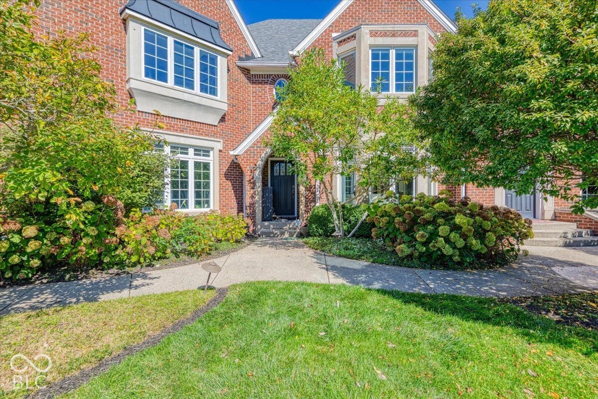 Brick exterior with multiple bay windows, black entry door, mature trees, and landscaped shrubbery