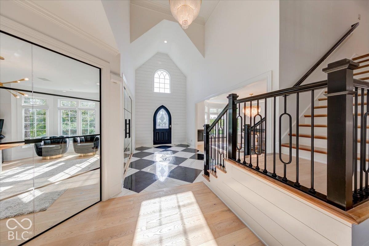 Two-story foyer featuring a black and white checkerboard floor, arched front door, an arched window, and a grand staircase with decorative metal balusters