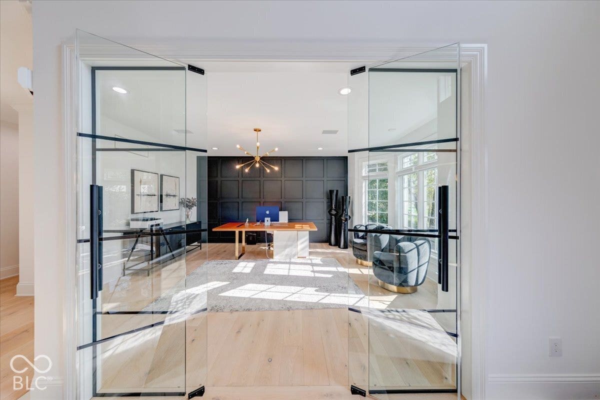 Double glass doors with black framing, light wood-finish flooring, and a decorative paneled accent wall