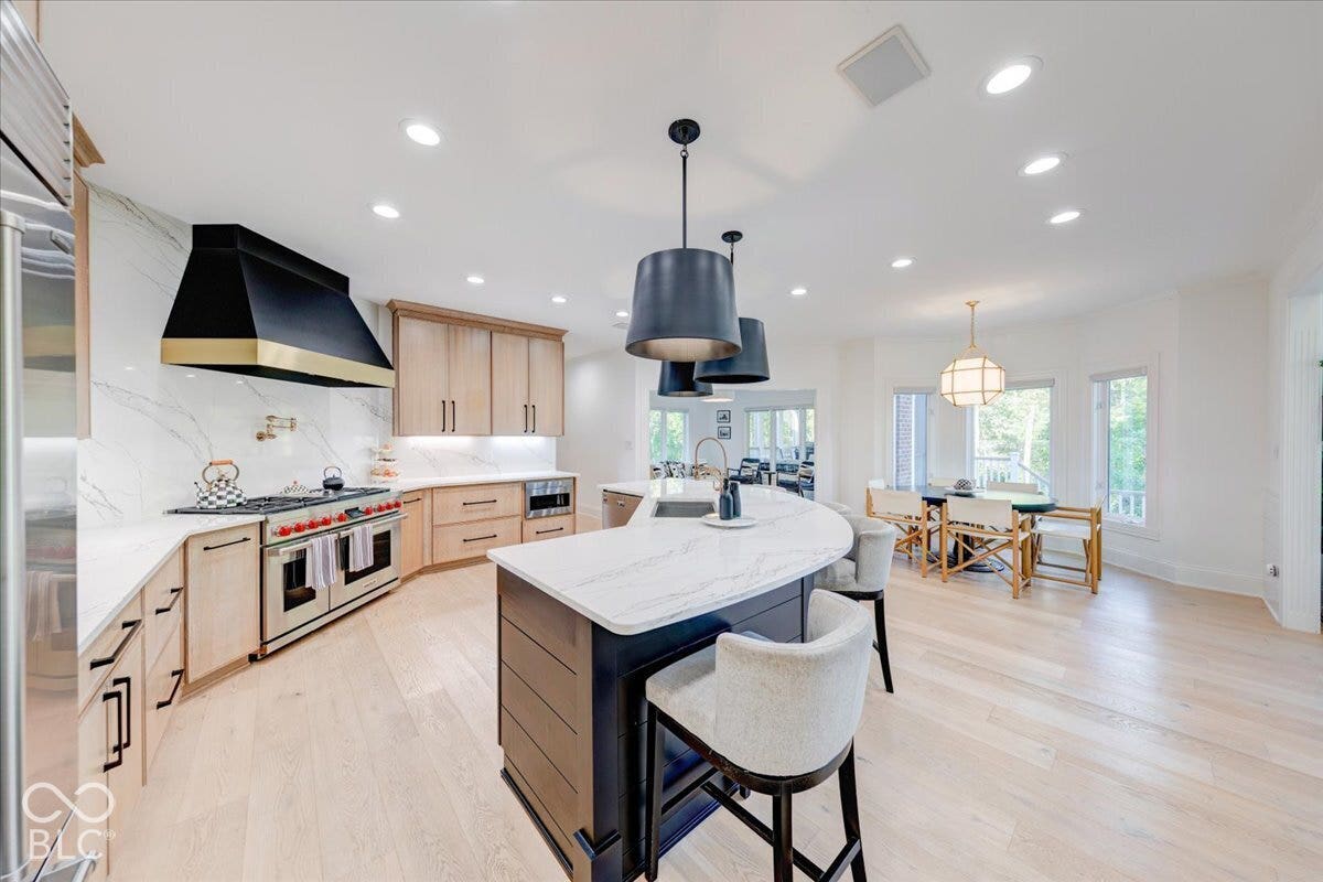Gourmet kitchen featuring a large range with a custom range hood, light wood-finish cabinetry, and a curved island with a stone countertop