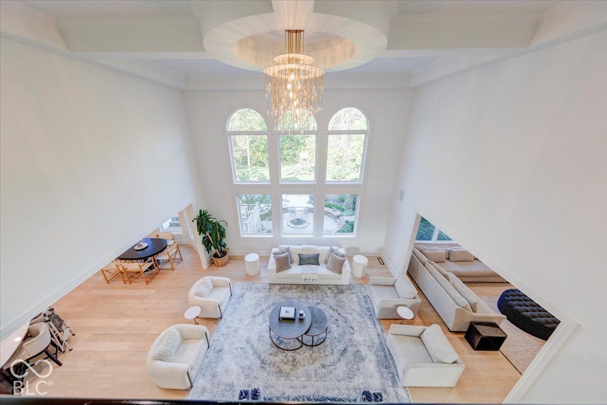 Vaulted ceiling with an ornate chandelier, multiple arched windows, hardwood flooring, and a large area rug