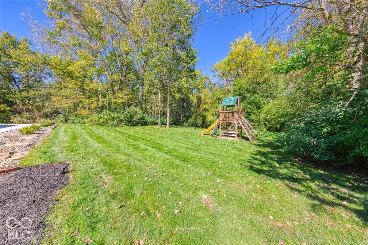 Expansive green lawn with mature trees and a wooden playset
