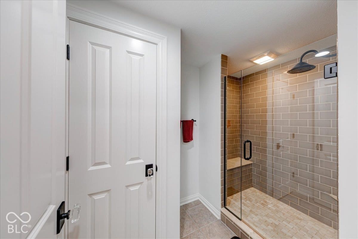 Glass-enclosed shower with subway tile surround, tiled shower floor, built-in shower bench, and dark-finish shower fixtures