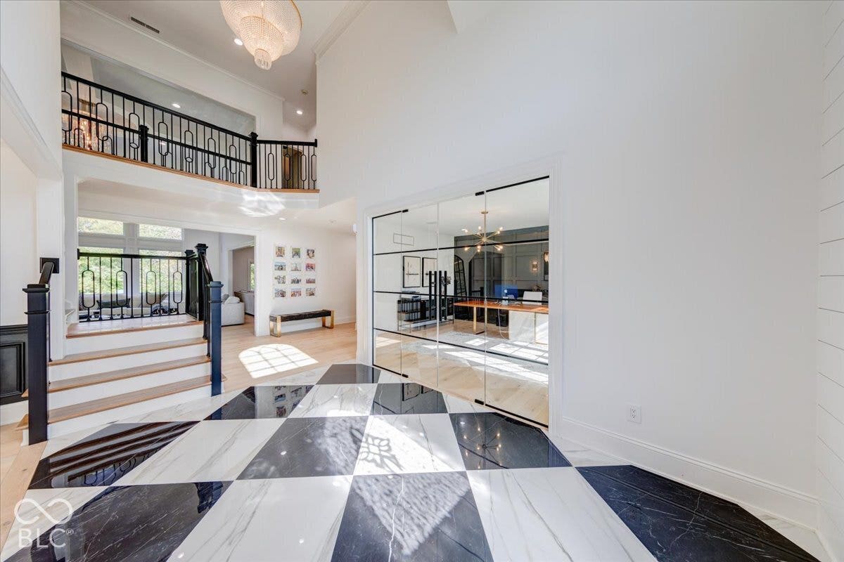 Two-story entry foyer with black and white checkered flooring, open staircase with black railings, and a glass-paneled room