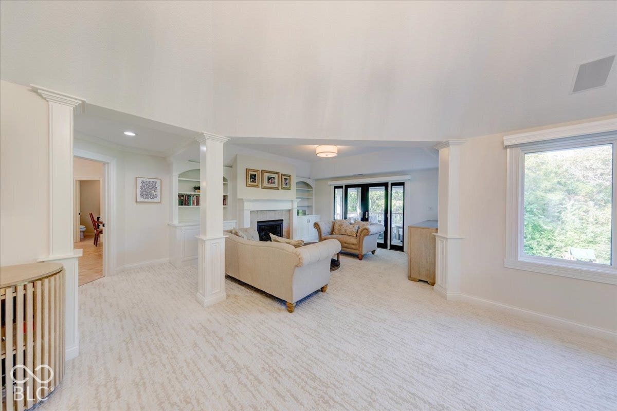 Spacious living area featuring light-toned carpet, a fireplace with a mantel, built-in shelving, and French doors