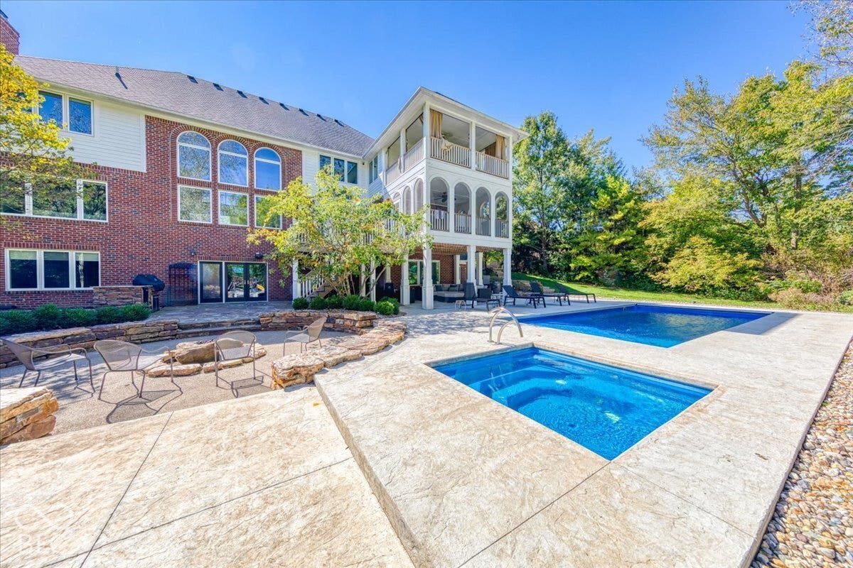 Brick and siding exterior with multiple arched windows, multi-level screened porches, stamped concrete patio, and a swimming pool with an integrated spa
