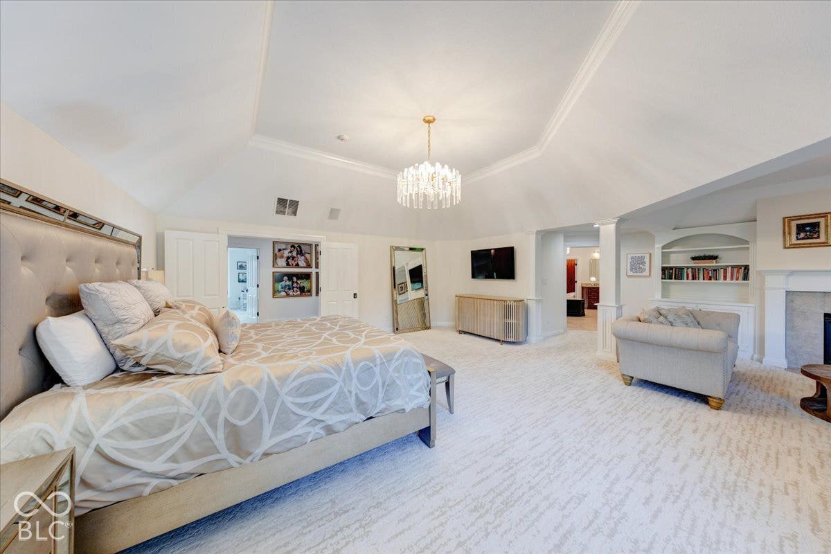 Vaulted ceiling with decorative trim, elegant chandelier, built-in shelving, and fireplace with mantel